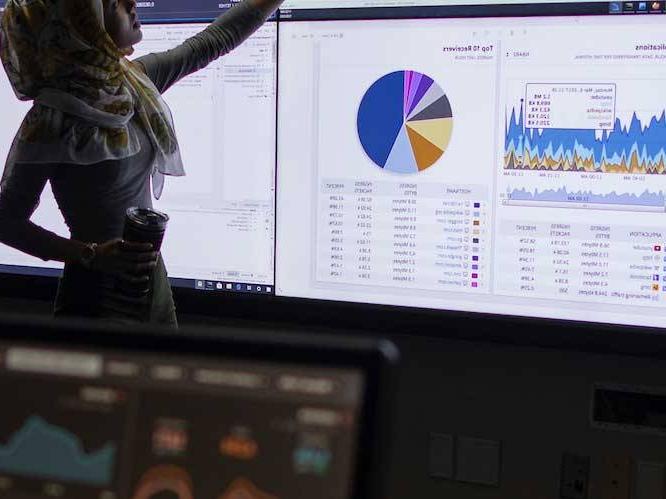 Woman standing infront of projector pointing to charts and graphs on the screen